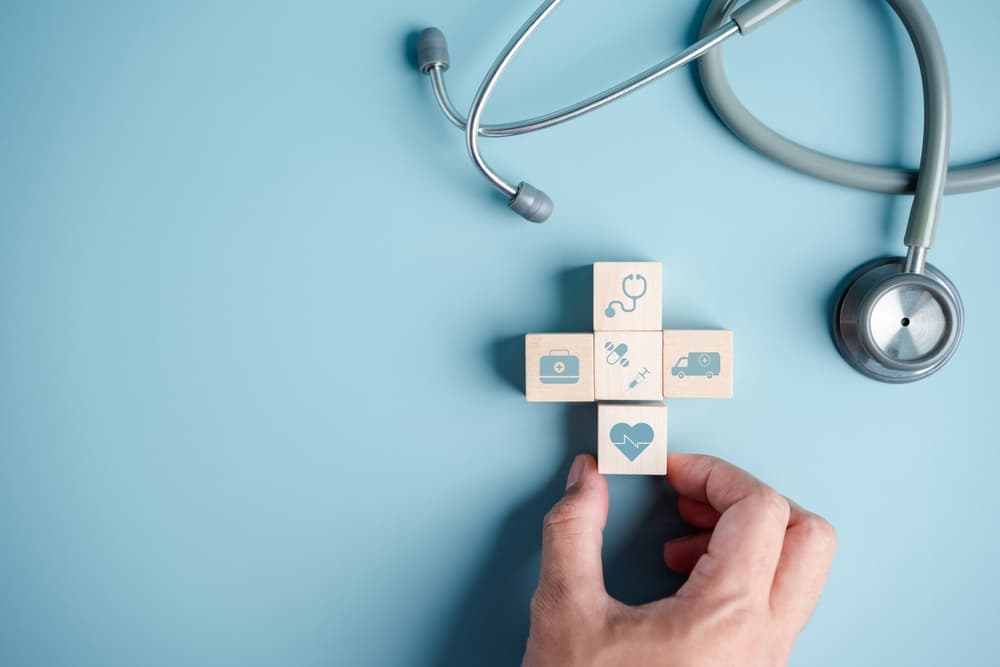 Concept of health insurance: hands arranging a plus symbol and healthcare blocks with a stethoscope, representing health and access to medical care.