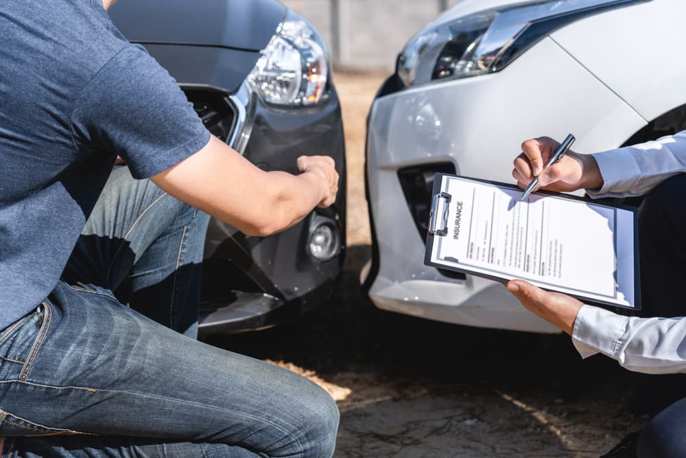 Agente de seguros revisando accidente de coche y cliente negociando, comprobando y firmando formulario de reclamación de informe tras colisión por accidente.
