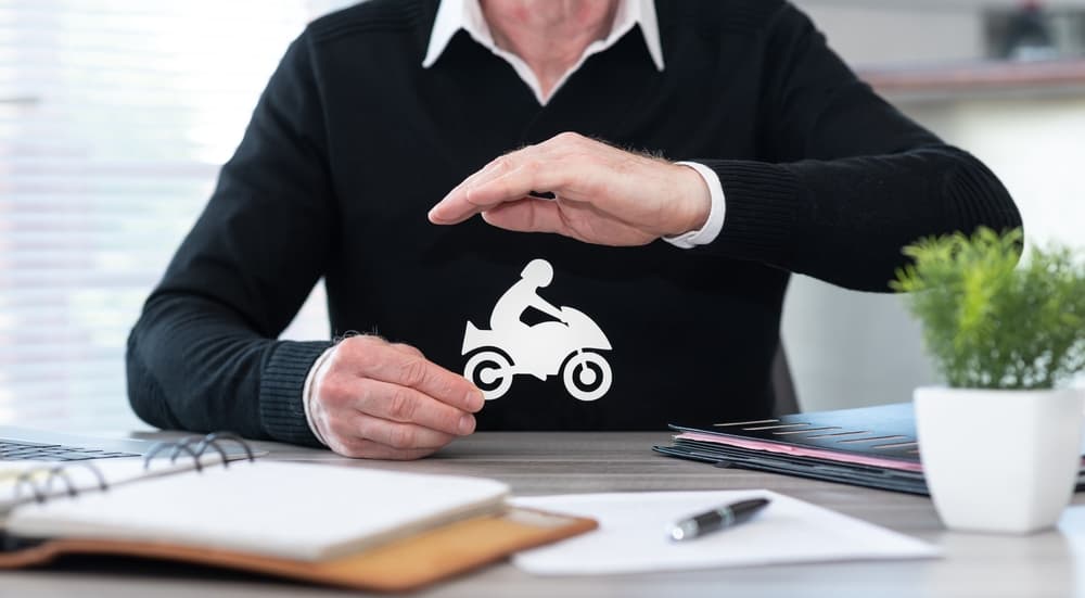 An insurer shields a motorbike with his hand, symbolizing protection and security.