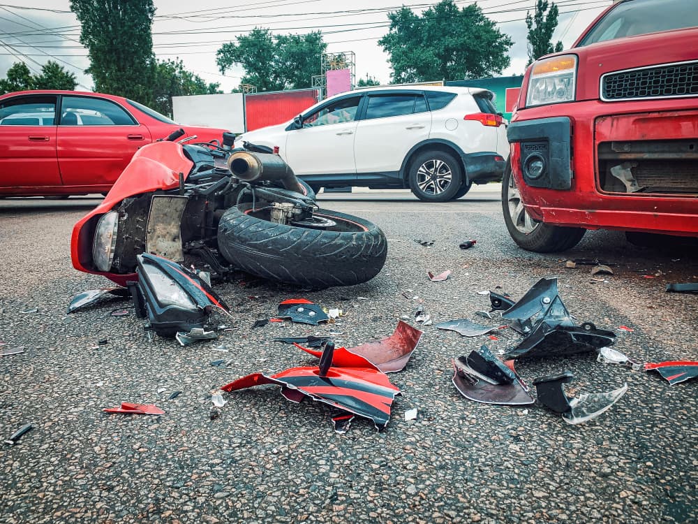 A motorcycle collided with a car, resulting in a wrecked bike lying broken on the road.