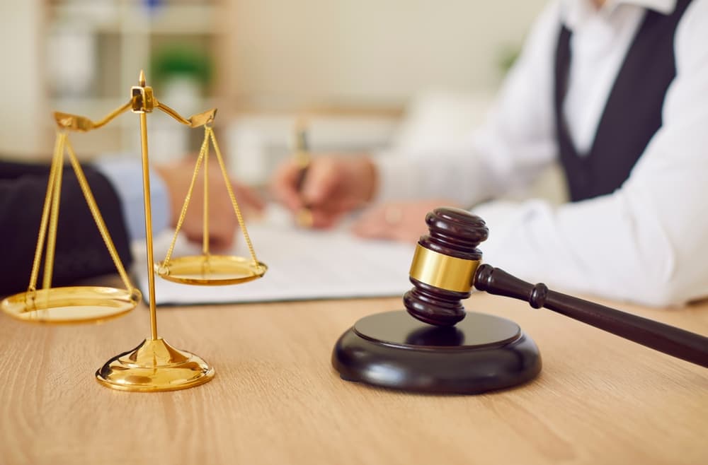 Close-up of golden scales of justice and wooden gavel on lawyer's office desk, with legal consultation in background. Legal advice and service concept.