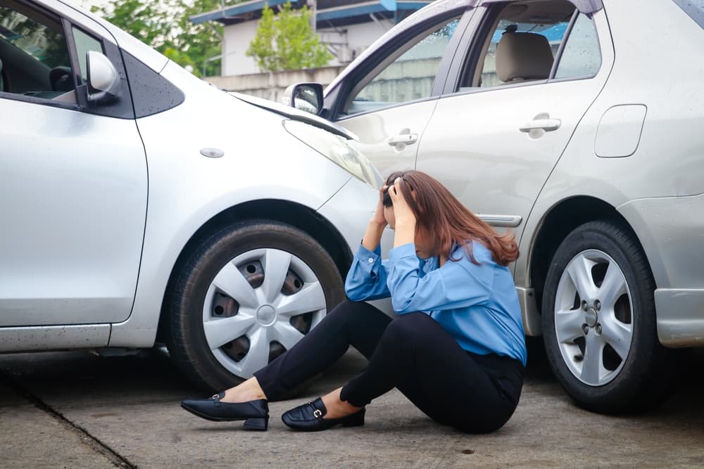 "Mujer estresada tras un accidente de coche, después de haber colisionado con otro vehículo en una carretera resbaladiza y mojada por la lluvia.