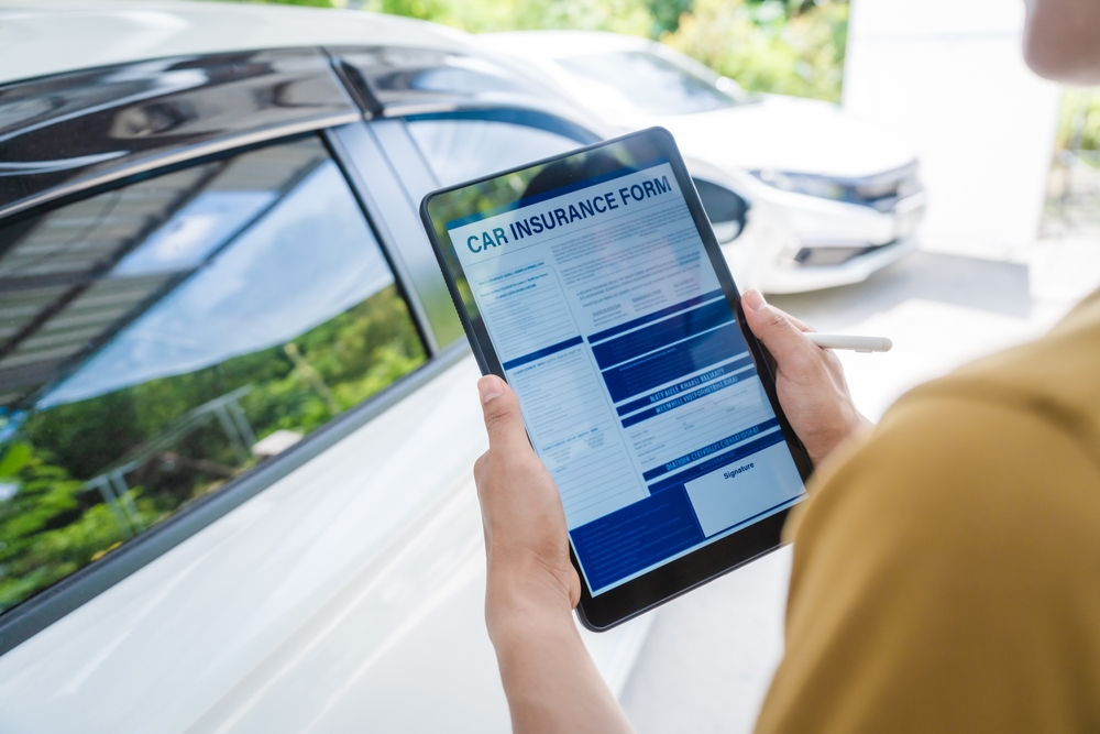 Man fills out a car insurance form after a car accident. Comprehensive motor insurance covers car damage. He files a claim report, speaking with an adjuster