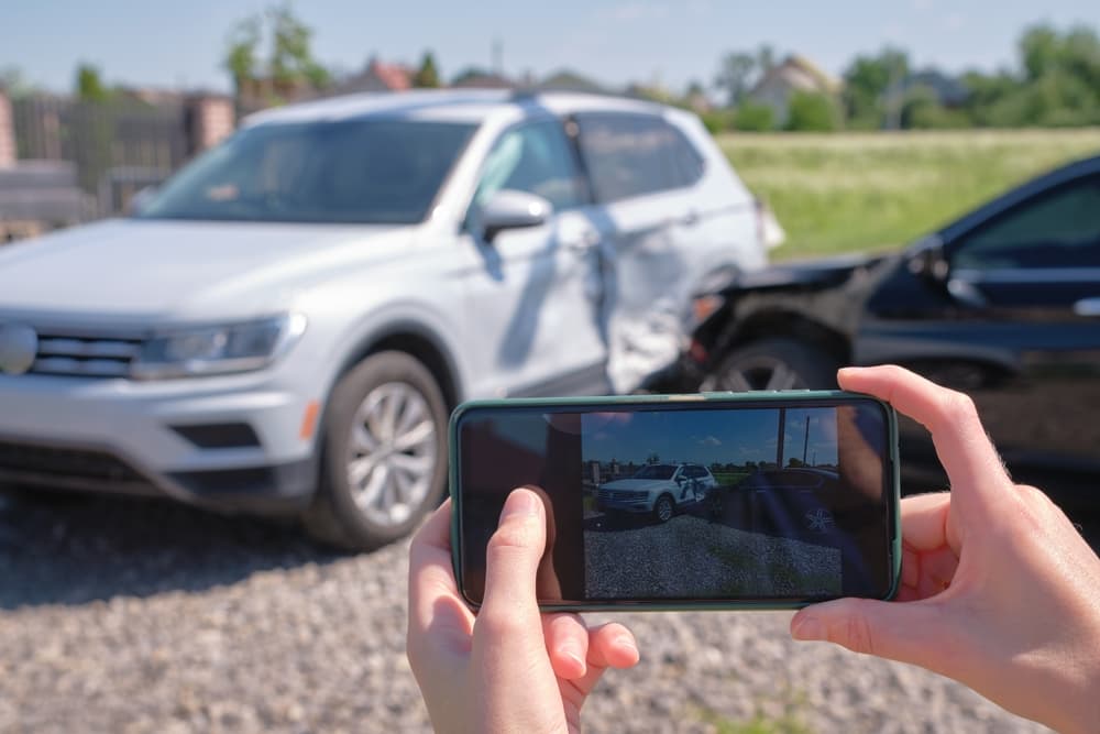 Driver taking a photo with a mobile phone after a vehicle collision on the roadside for emergency services following a car accident