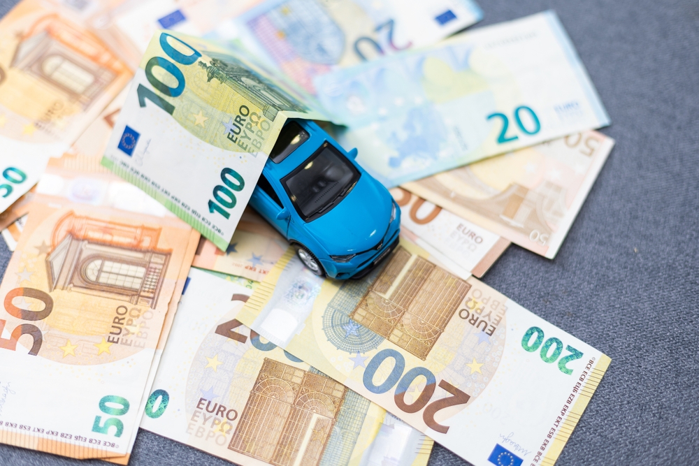 A toy car placed on top of scattered euro banknotes, symbolizing car expenses.