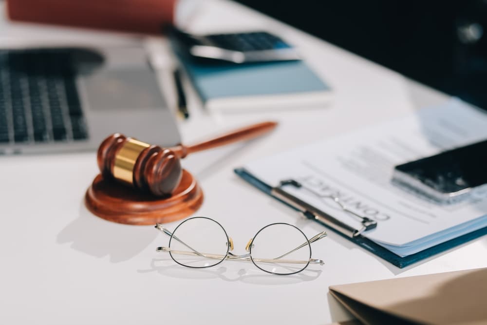 Abogado revisando documentos contractuales con un mazo de madera sobre la mesa en un tribunal, representando la justicia, la ley y los procedimientos legales.