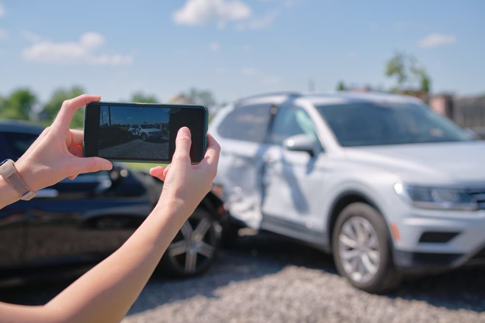 Female driver taking photos of a car accident for insurance purposes.