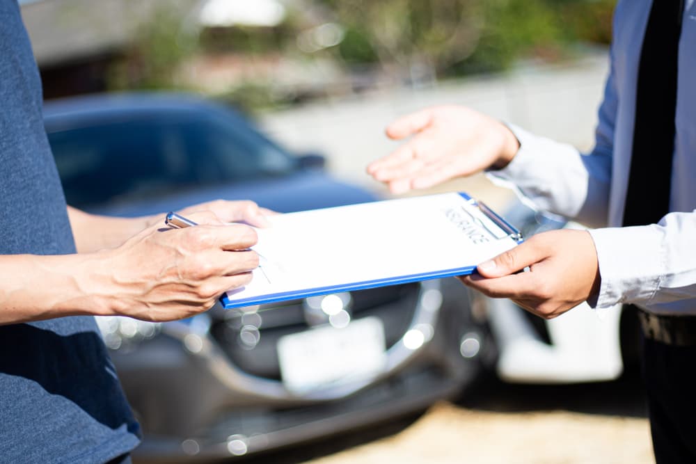 Clientes y agentes de seguros firman documentos para reclamar una indemnización tras un accidente de coche, lo que pone de relieve el proceso del seguro.