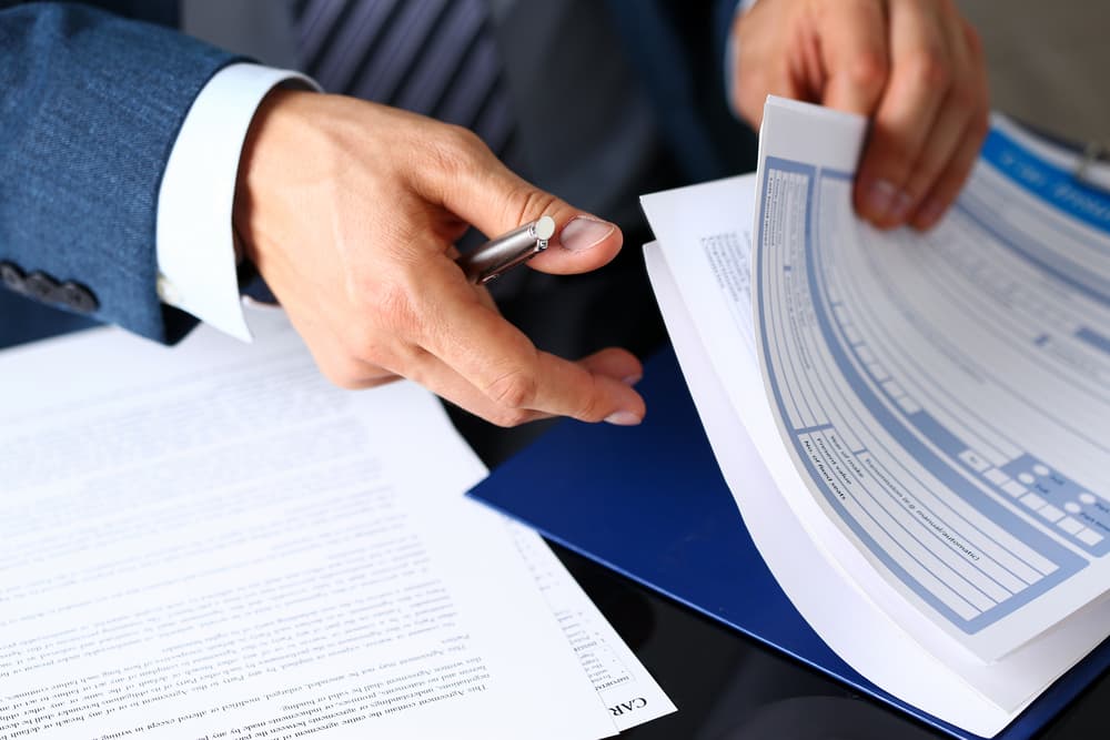 A person in a suit reviewing and signing legal documents with a pen.