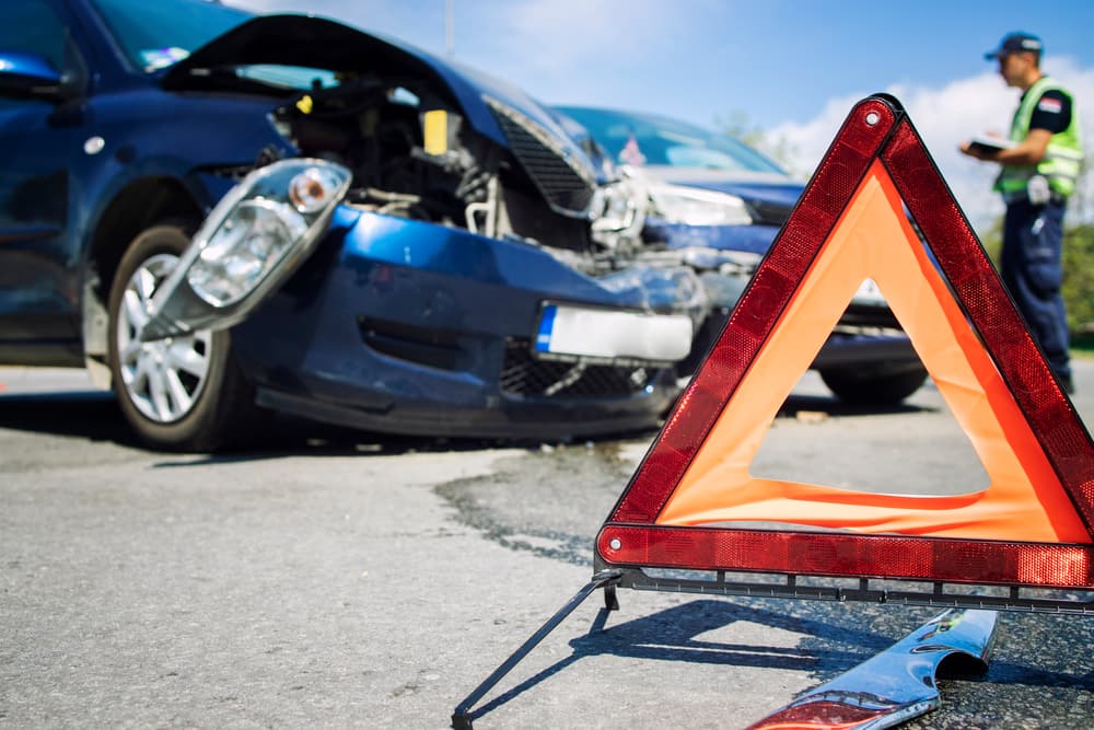 A red warning triangle placed near a car accident scene with a police officer nearby.