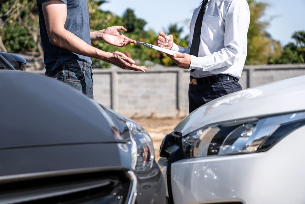 Insurance agent reviewing a car crash report and negotiating with a customer, signing the claim form after an accident.