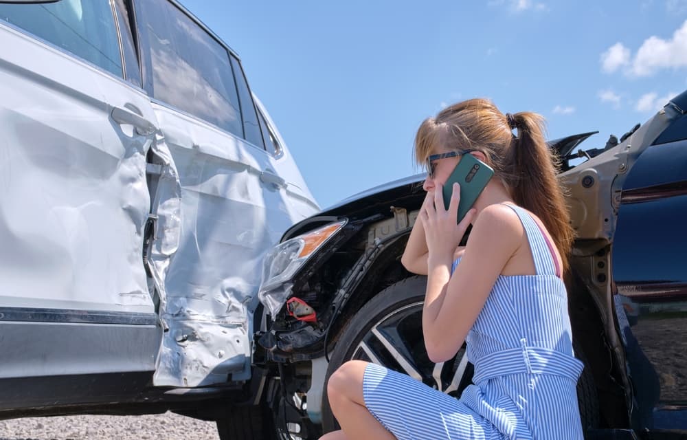 Una mujer hablando por teléfono sentada junto a dos coches con importantes daños por colisión.