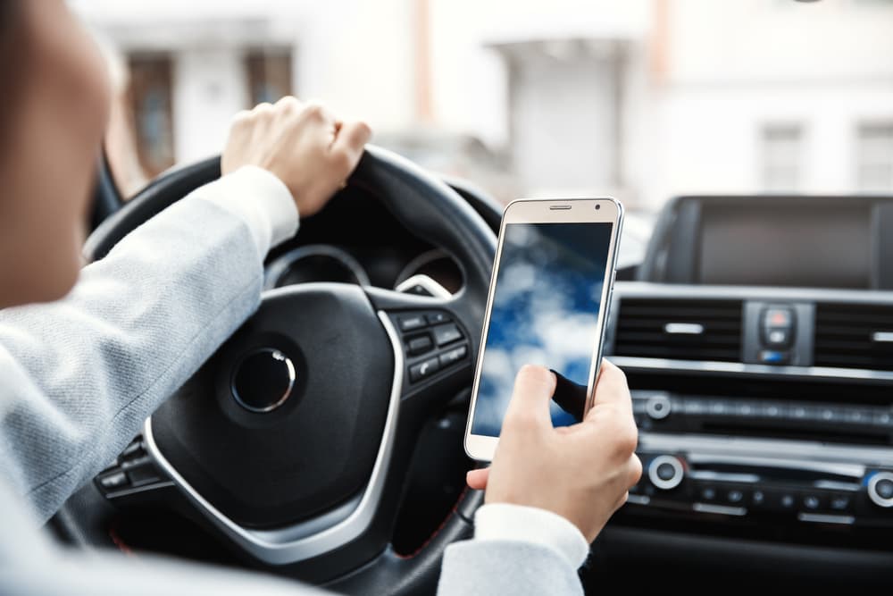 Young female driver using smartphone in car, checking road app and texting while parked.