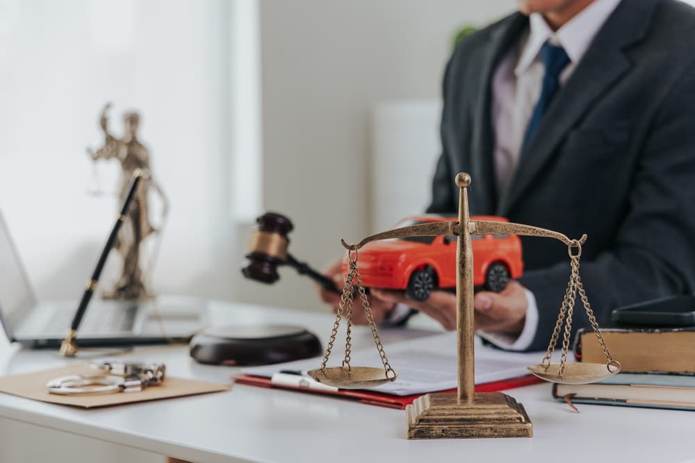 Judge's hand with a car model, documents, and gavel, symbolizing legal proceedings in a car accident case.