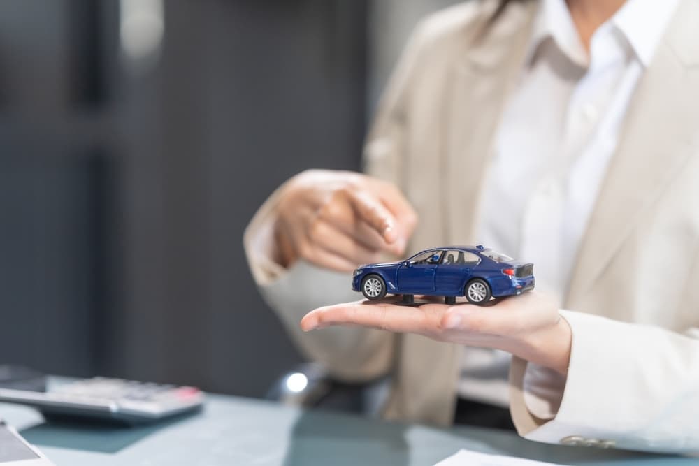 A person holding a miniature blue car, explaining insurance details at a desk.