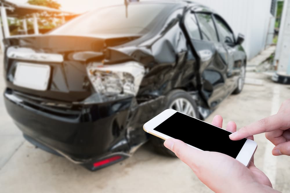 Accident victim making a call for assistance after a car crash, with a damaged vehicle in the background