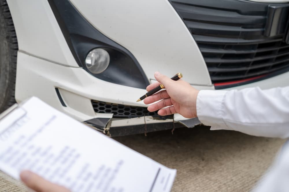 Un inspector señala los daños de un coche mientras sostiene un portapapeles con los detalles de la inspección.