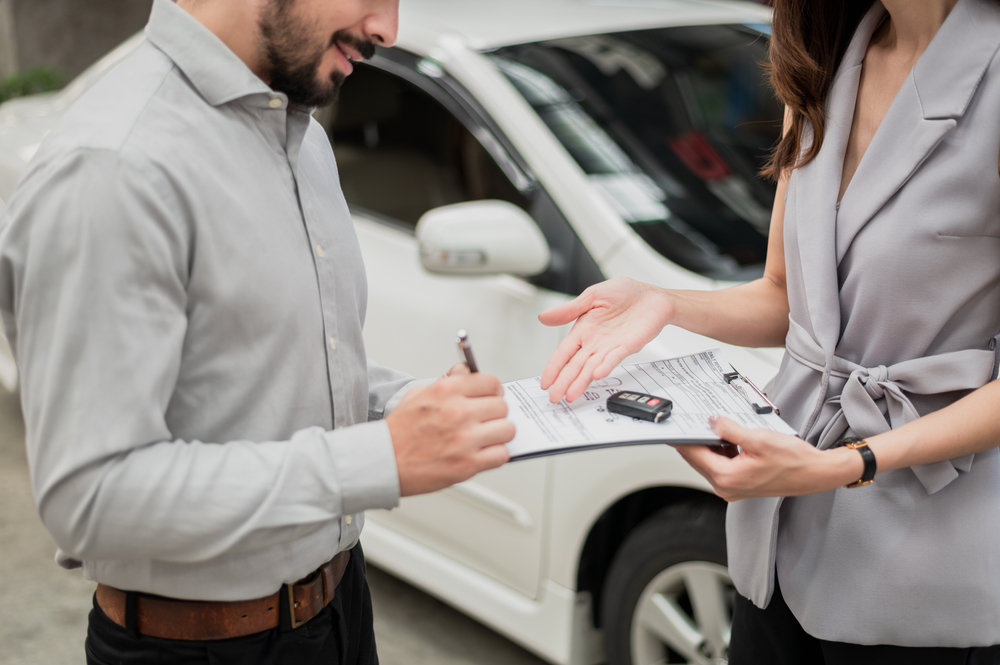 Negocio de la automoción, concepto de seguro de coche: Cliente feliz finalizando un trato y firmando un contrato de seguro con un agente de seguros de coche.