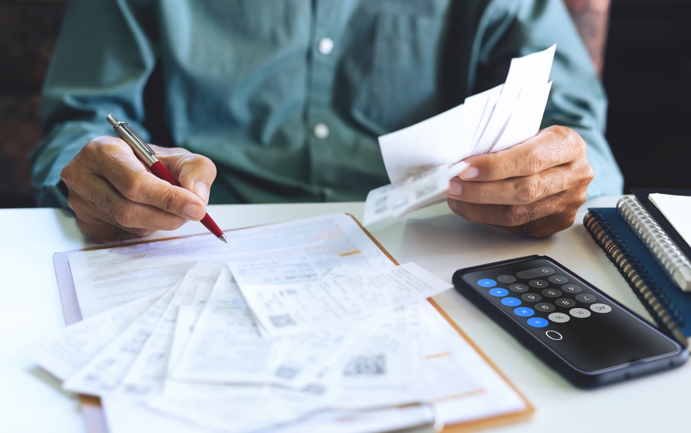 Stressed Asian man using a smartphone to document expenses related to a personal injury.