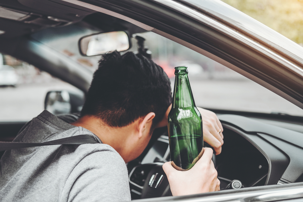 Hombre borracho conduciendo un coche por la carretera mientras sostiene una botella de cerveza. Peligroso concepto de conducción en estado de embriaguez.