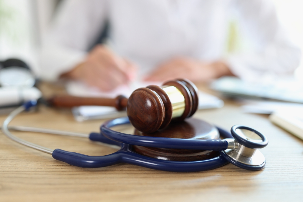 Close-up of a judge's gavel and a doctor's stethoscope on an office desk. Concept of medical malpractice, personal injury law, and healthcare legal issues.